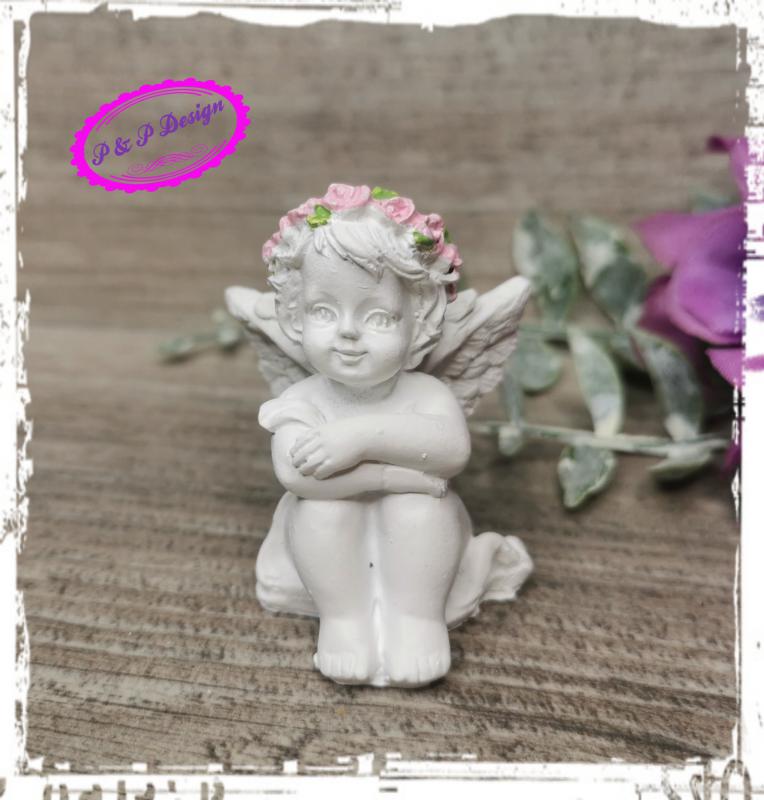 Angyalka ülő, M4,5 cm, rózsaszín virágkoszorú a fején - kezei a térdén