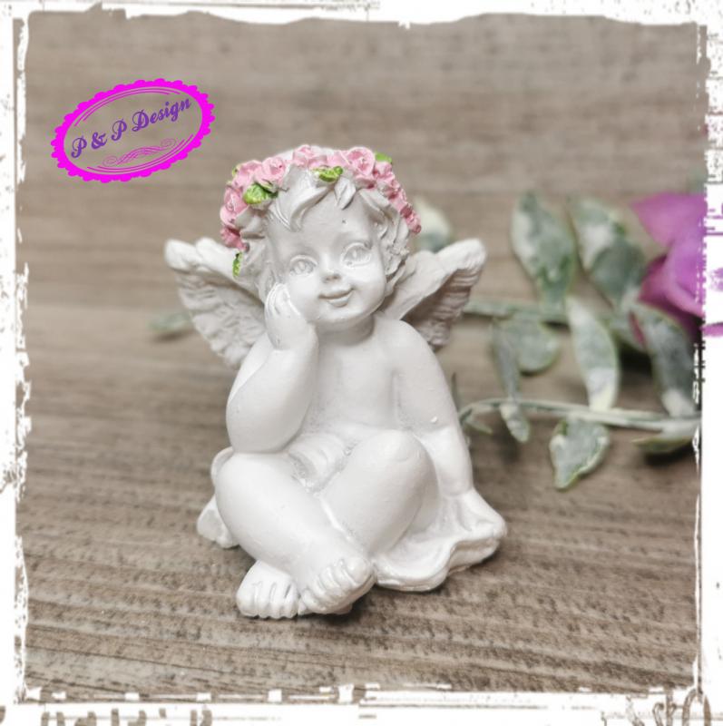 Angyalka ülő, M4,5 cm, rózsaszín virágkoszorú a fején - szemből bal kéz az arcánál